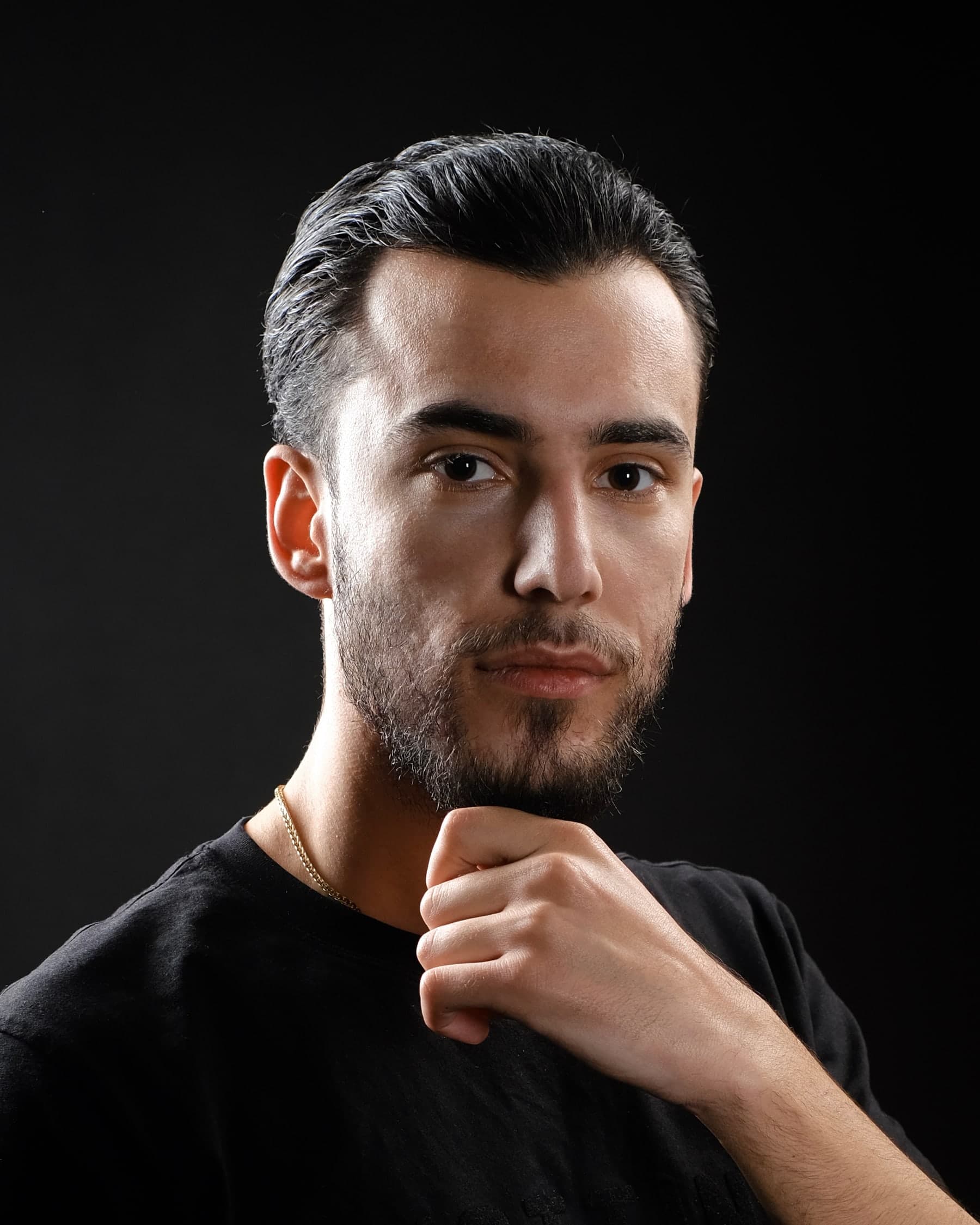 Portrait of Orgito Baraj resting his chin on his hand against a black background